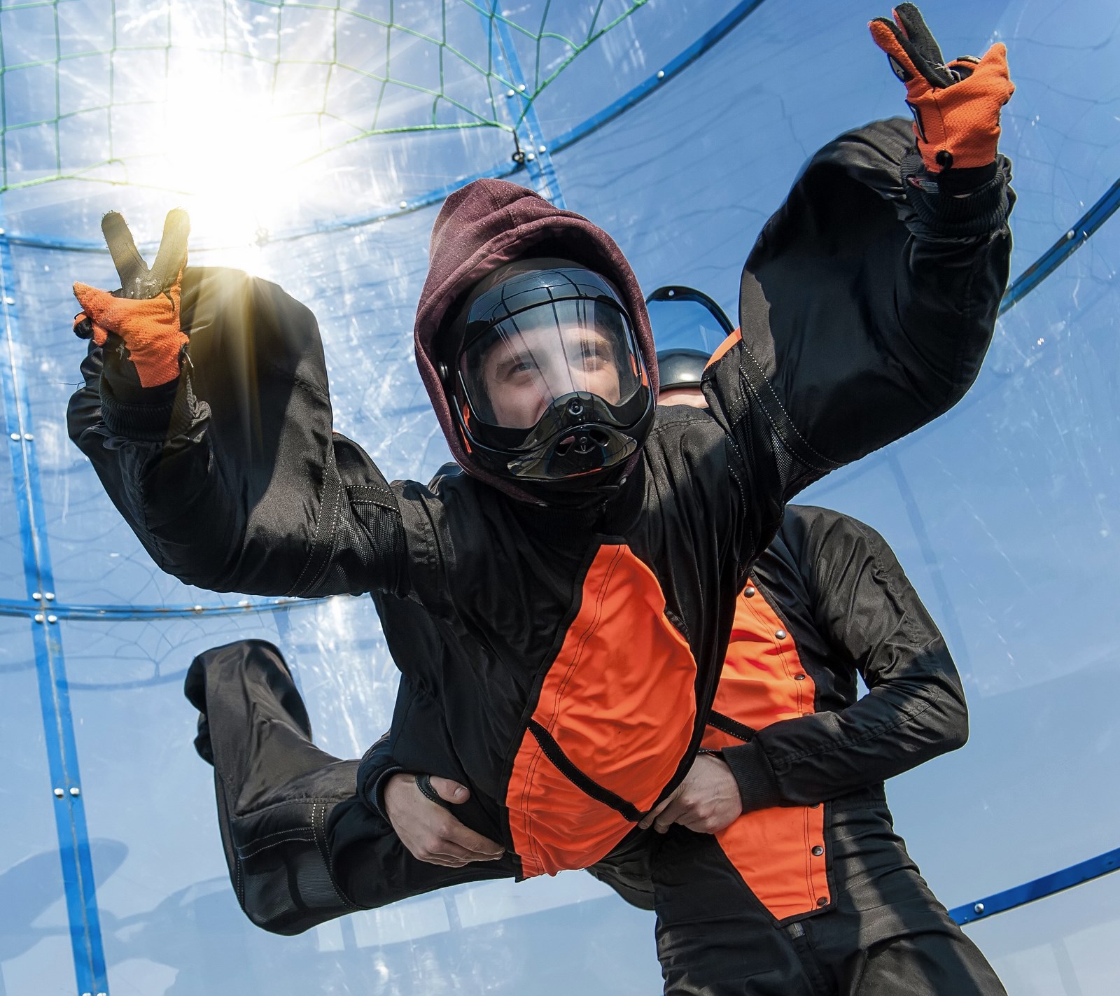 Osoba ubrana w kombinezon do latania unosi się w tunelu aerodynamicznym, przy czym towarzyszy jej operator.