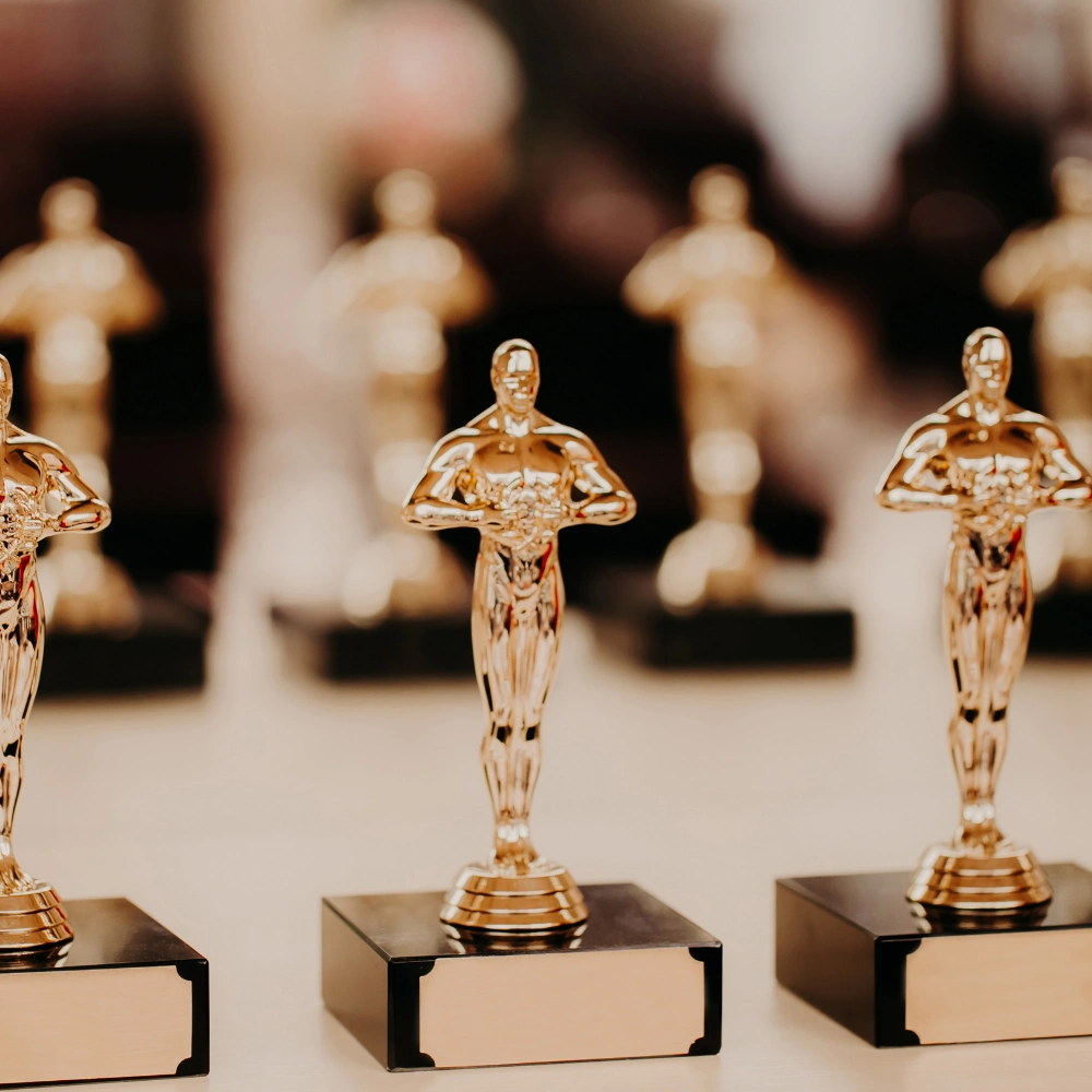 Na zdjęciu znajduje się kilka złotych statuetek ustawionych w rzędzie, przypominających nagrody filmowe.