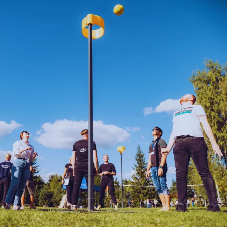 Grupa ludzi gra w kornhole na świeżym powietrzu pod niebieskim, bezchmurnym niebem.