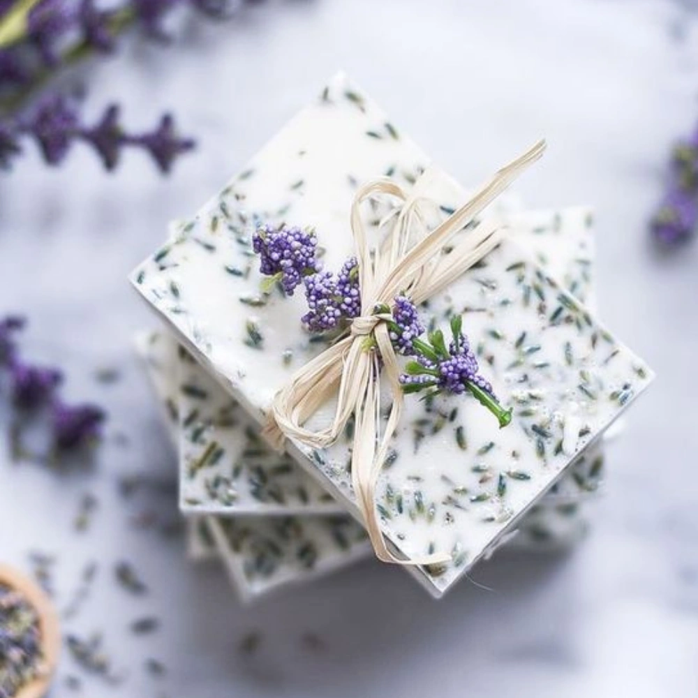 Grafika przedstawia stos lawendowych mydełek ozdobionych suszoną lawendą i związanych sznurkiem.