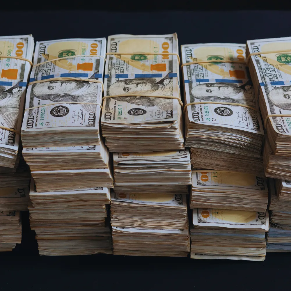 Stosy banknotów dolarowych, związanych gumkami, leżą na ciemnej powierzchni.