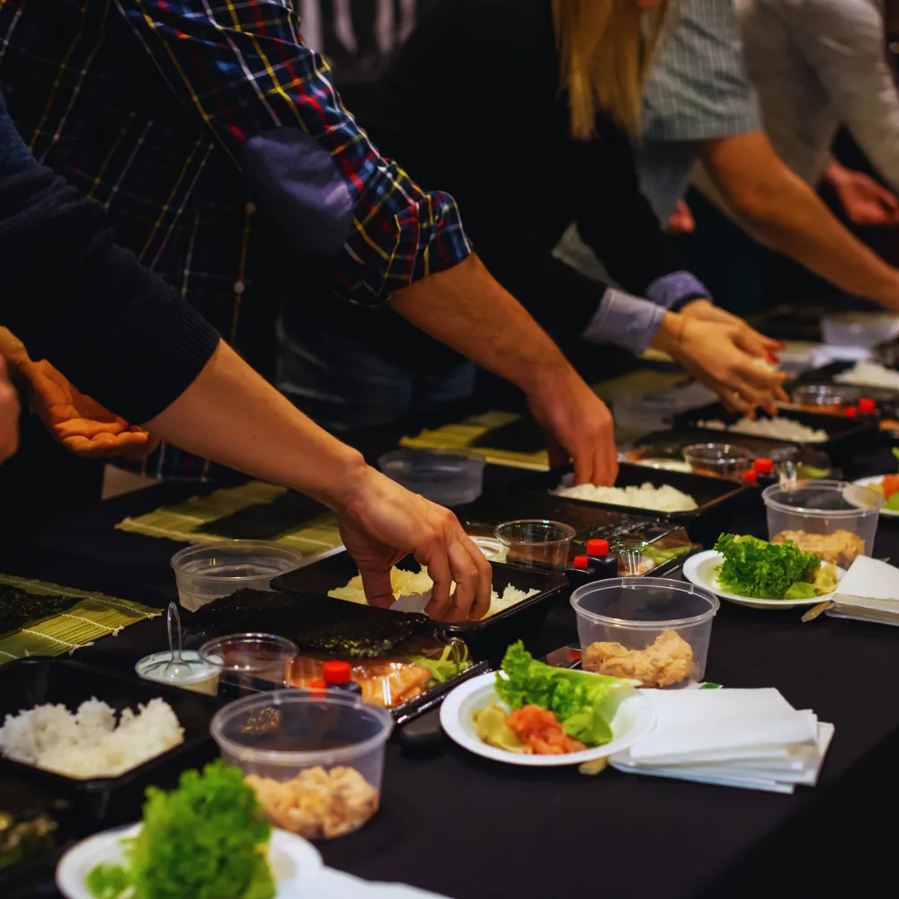 Na zdjęciu widać ludzi uczestniczących w warsztatach kulinarnych, prawdopodobnie przygotowujących sushi, co może być jedną z atrakcji oferowanych przez organizatorów Mistrzowie Imprez.