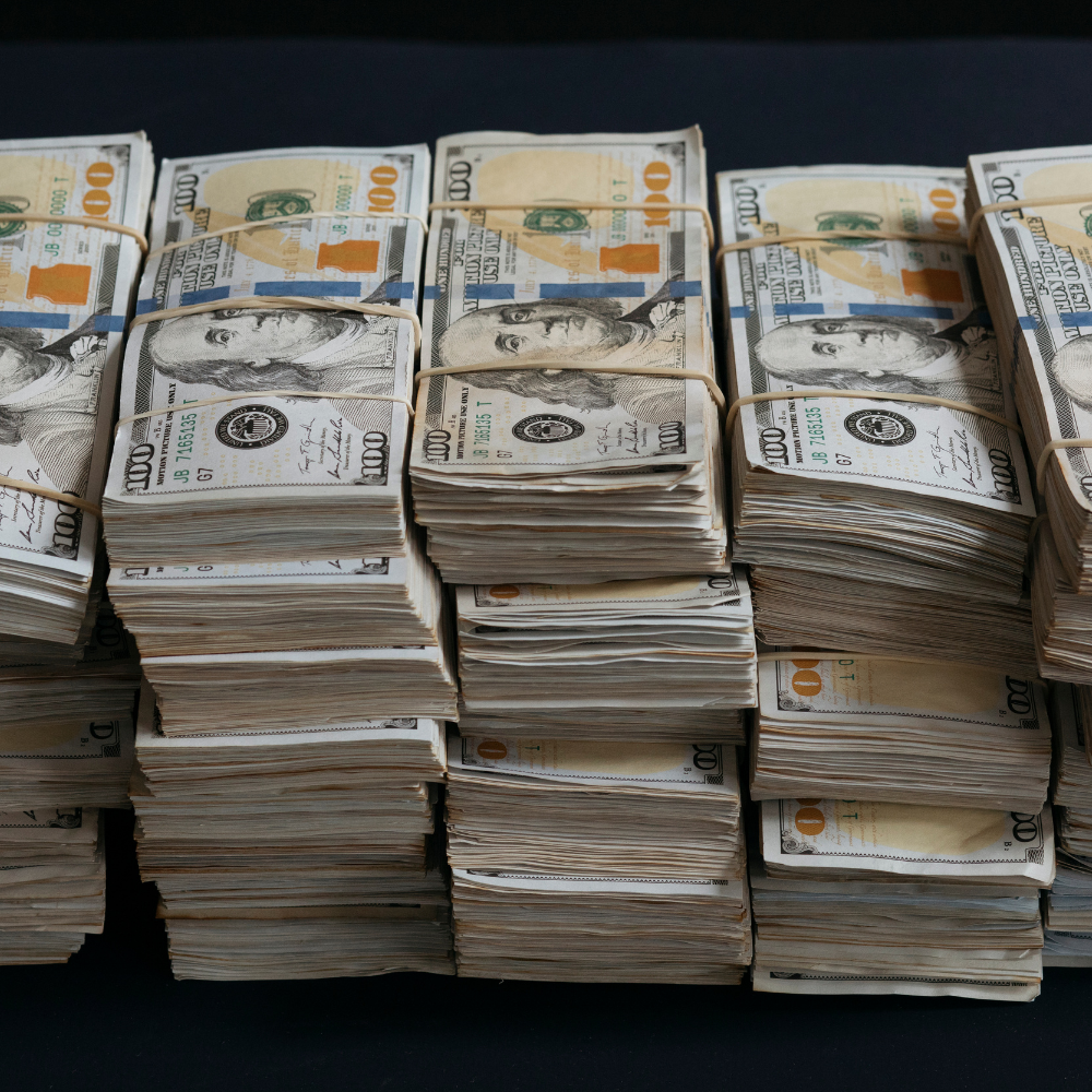 Stosy banknotów o nominale 100 dolarów są ciasno związane gumkami, ułożone w rzędach.